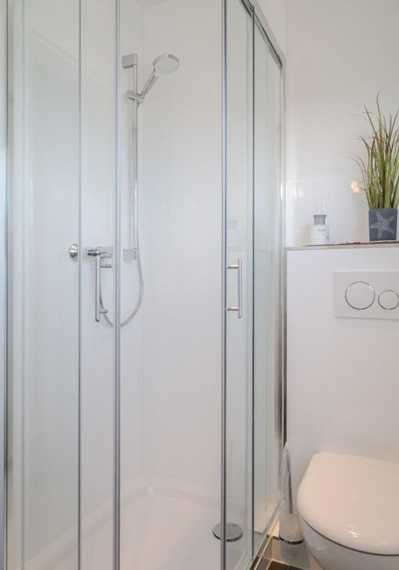 Duschbad der Ferienwohnung mit verglaster Eckduschkabine, WC und maritimer Dekoration