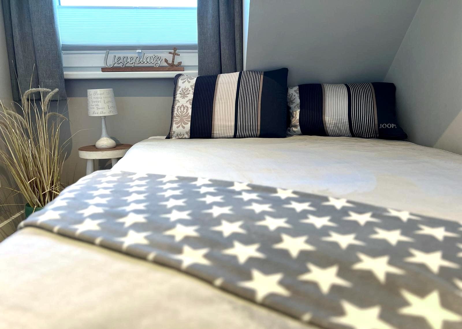 Schlafzimmer der Ferienwohnung mit Doppelbett aus Eiche, blau-weißen Kissen, Sternendecke und Nachttischlampe
